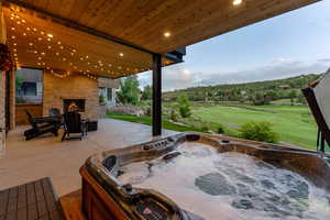 View of patio featuring an outdoor stone fireplace, a hot tub, and golf course view