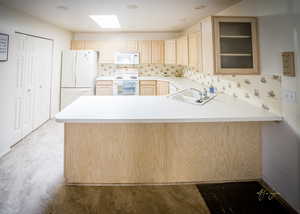 Kitchen with white appliances, a peninsula, a sink, decorative backsplash, and glass insert cabinets