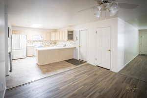 Kitchen featuring decorative backsplash, a peninsula, wood finished floors, white appliances, and a ceiling fan