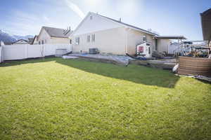 Rear view of property with brick siding, a lawn, cooling unit, and a fenced backyard