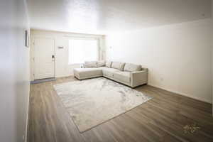 Unfurnished living room featuring wood finished floors, baseboards, and a textured ceiling