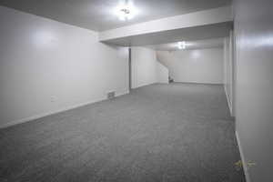 Finished basement with visible vents, carpet floors, baseboards, and stairway