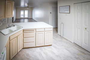 Kitchen featuring light brown cabinets, light countertops, a peninsula, a ceiling fan, and a sink