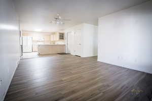 Unfurnished living room featuring baseboards, dark wood-style flooring, and a ceiling fan