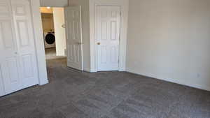 Unfurnished bedroom featuring washer / dryer, baseboards, dark colored carpet, and a closet