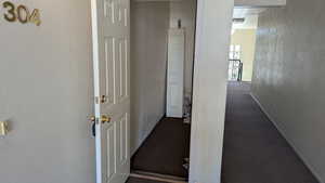 Corridor featuring baseboards, dark carpet, and a textured wall