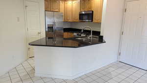 Kitchen with dark countertops, light tile patterned floors, appliances with stainless steel finishes, a peninsula, and a sink