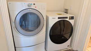 Clothes washing area with light tile patterned floors, laundry area, and washing machine and clothes dryer