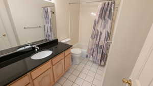 Bathroom with tile patterned floors, toilet, shower / tub combo with curtain, and vanity