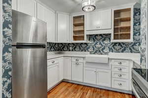 Kitchen with wallpapered walls, light wood-style flooring, freestanding refrigerator, a sink, and white cabinets