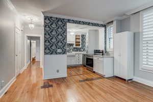 Kitchen with light wood-type flooring, ornamental molding, electric stove, plenty of natural light, and wainscoting