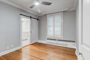 Spare room with a ceiling fan, wood finished floors, a barn door, radiator, and crown molding