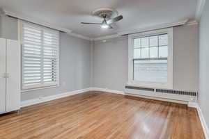 Spare room with radiator, a ceiling fan, baseboards, light wood finished floors, and crown molding