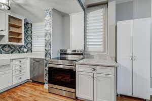 Kitchen featuring light wood-type flooring, appliances with stainless steel finishes, white cabinets, glass insert cabinets, and light stone countertops