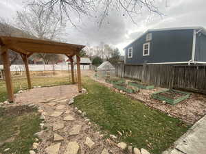 View of yard featuring an outbuilding, a pergola, a fenced backyard, a greenhouse, and a garden