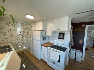 Kitchen with a sink, wood finished floors, white appliances, white cabinets, and decorative backsplash