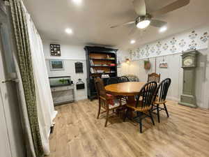 Dining area with light wood-style floors, wainscoting, and a ceiling fan
