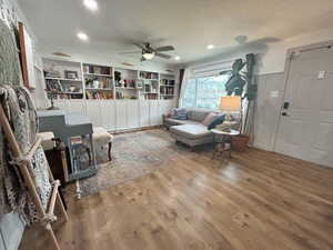 Living area with built in features, wood finished floors, a wainscoted wall, recessed lighting, and ceiling fan