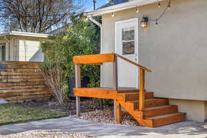 Back entry to the laundry room featuring new stairs and newer landscaping.