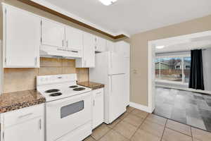 Kitchen featuring under cabinet range hood, white appliances, backsplash, and white cabinets