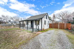 View of front of home with a porch, gravel driveway, roof with shingles, and fence