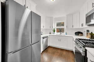 Kitchen with a sink, dark wood finished floors, stainless steel appliances, white cabinets, and light countertops