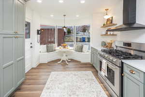 Kitchen with stainless steel range with gas cooktop, wood finished floors, light countertops, and wall chimney range hood