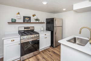 Kitchen featuring a sink, open shelves, wood finished floors, appliances with stainless steel finishes, and light countertops