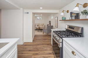 Kitchen with wood finished floors, gas stove, visible vents, white cabinets, and a textured ceiling