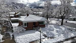 Snow covered back of property with brick siding, a chimney, and a tile roof