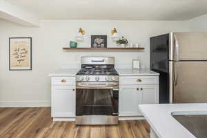 Kitchen featuring open shelves, wood finished floors, light countertops, and appliances with stainless steel finishes