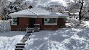 Snow covered back of property with a tile roof, fence, a mountain view, brick siding, and a chimney