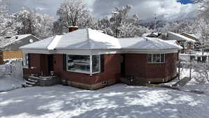 View of snow covered exterior featuring brick siding, a tile roof, and a chimney