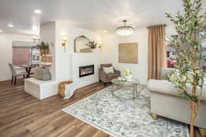 Living room featuring a notable chandelier, a glass covered fireplace, wood finished floors, recessed lighting, and baseboards