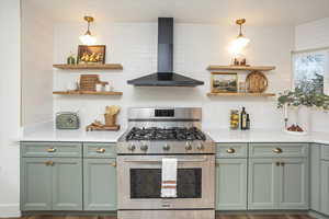 Kitchen with green cabinets, open shelves, wall chimney exhaust hood, and stainless steel gas range