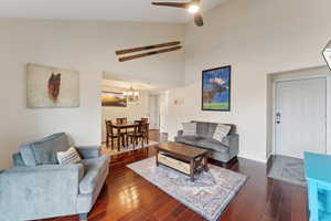 Living room featuring baseboards, high vaulted ceiling, dark wood-style flooring, and ceiling fan with notable chandelier