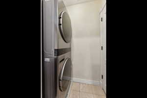 Laundry room featuring laundry area, light tile patterned floors, baseboards, and stacked washer and clothes dryer