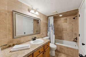 Bathroom featuring tile walls, toilet, vanity, a textured ceiling, and tiled shower / bath