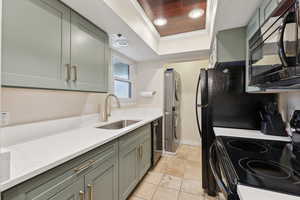 Kitchen featuring black appliances, ornamental molding, a sink, light tile patterned flooring, and a raised ceiling