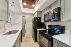 Kitchen featuring ornamental molding, a sink, black appliances, light countertops, and a raised ceiling