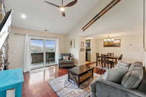 Living area with visible vents, ceiling fan with notable chandelier, wood finished floors, baseboards, and lofted ceiling