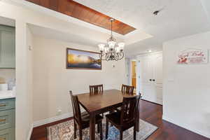 Dining room featuring a chandelier, baseboards, a raised ceiling, and dark wood-type flooring