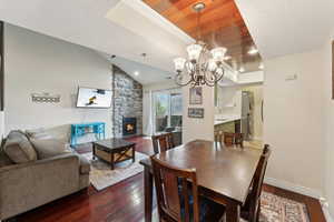 Dining area with dark wood-style floors, baseboards, an inviting chandelier, lofted ceiling, and a raised ceiling