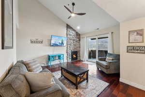 Living area featuring wood finished floors, visible vents, high vaulted ceiling, ceiling fan, and a stone fireplace