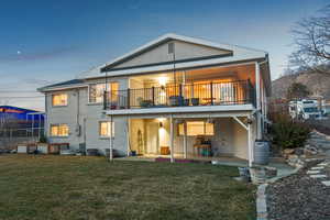 Rear view of house featuring a balcony, a yard, central air condition unit, a patio area, and brick siding