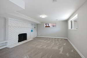 Basement with visible vents, a brick fireplace, baseboards, and carpet floors