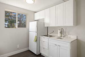 Kitchen with baseboards, light countertops, freestanding refrigerator, white cabinets, and a sink