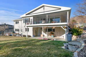 Back of house with brick siding, fence, a lawn, a balcony, and a patio