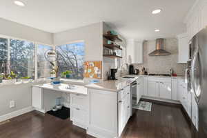 Kitchen with dark wood finished floors, open shelves, a sink, appliances with stainless steel finishes, and wall chimney exhaust hood