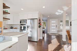 Kitchen with tasteful backsplash, white cabinets, appliances with stainless steel finishes, and open shelves